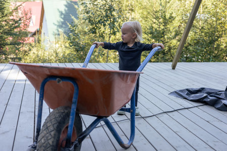 A young child enjoys pushing a vibrant wheelbarrow on a wooden deck, surrounded by construction...