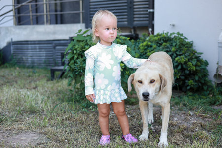 A small child stands confidently in a backyard, wearing a light green dress adorned with white...