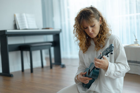 Sitting on a wooden floor in a well-lit space, a musician in casual attire plays a ukulele while...