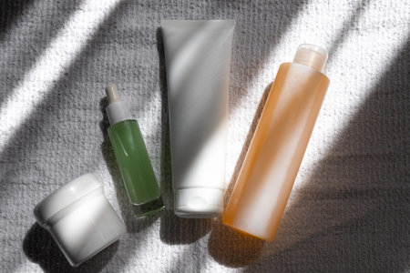 A selection of skincare products is neatly arranged on a textured surface, illuminated by gentle...