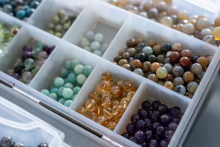 Various types of colorful beads are neatly arranged in compartments of a clear storage box. Container of Natural Stone Bead Chips For Jewelry Making. Hobbies, relax and lithotherapy conceptの写真素材