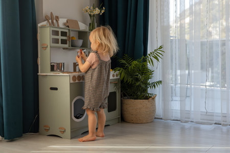A young child stands at a small kitchen set, pretending to cook in a bright and airy room. Eco-friendly and safe handmade wooden products for children development and learning.の写真素材
