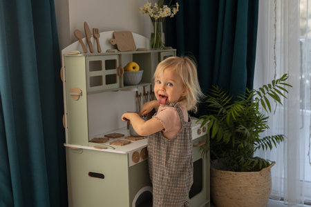 Young child happily stirs a pot in a colorful toy kitchen set. Sunlight filters through the window. Eco-friendly and safe handmade wooden products for children development and learning.の写真素材