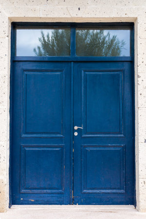 A vibrant blue wooden retro door with two panels and a window above stands against a textured stone...