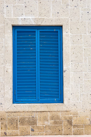 Blue shutters complement a light-colored stone wall, showcasing architectural details in a serene...