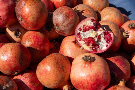 Bright red pomegranates fill a market stall, showcasing their shiny skins and vibrant color. A cut...