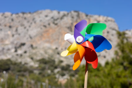 Brightly colored pinwheel is spinning joyfully in the breeze, set against a stunning mountainous landscape and blue skyの写真素材