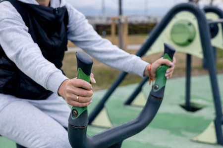 Close-up of female hands. Person in activewear utilizes outdoor fitness equipment in a park on a bright day. The equipment is designed for exercise, promoting health and well-being in the community.の写真素材