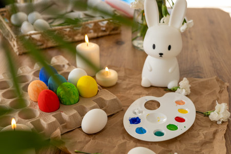 A lively display of decorated Easter eggs arranged around a bunny figurine. The palette, filled with vibrant paints, is ready for creativity, while candles add a warm glow.の写真素材