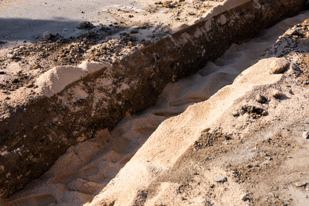 A deep trench has been dug into the ground at a construction site, revealing layers of sand and...