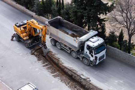 A construction crew is actively repairing the street using a digging machine and a dump truck. Road repair or pipe replacement. Aerial viewの写真素材