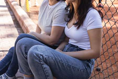 Two women mother and daughter are seated beside each other on a concrete surface, enjoying a moment...
