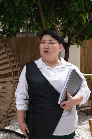 Young business woman overweight stands in a lush garden filled with greenery, wearing a white shirt....