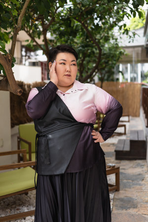 A young beautiful brunette plus-size Asian woman poses with confidence in a fashionable outfit while surrounded by greenery. Body positive and lifestyleの写真素材