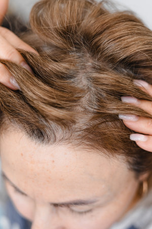Mature middle-aged caucasian woman touching her gray, silver roots hair close-up on gray tiles background, hair loss and age-related changes, naturalness and natural aging concept.の写真素材