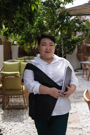 Young business woman overweight stands in a lush garden filled with greenery, wearing a white shirt....