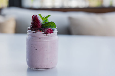 A jar filled with creamy strawberry home made yogurt sits on a table. It is decorated with fresh mint and ripe strawberries. The setting is bright and inviting, perfect for a light snack.の写真素材
