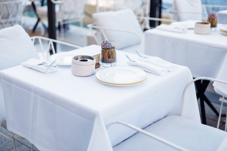 A beautifully arranged dining table features a crisp white tablecloth with elegant tableware,...