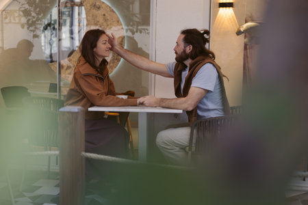 In cozy cafe setting, a man gently touches the face of woman as they share smiles. The atmosphere is relaxed, with soft lighting and modern decor enhancing their intimate moment.の写真素材