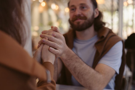 A man with a beard chats with someone in a relaxed cafe setting. He sits at a table with a candle,...