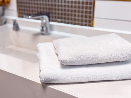 Fresh white towels sit on a sleek countertop in a contemporary bathroom. The minimalist design...