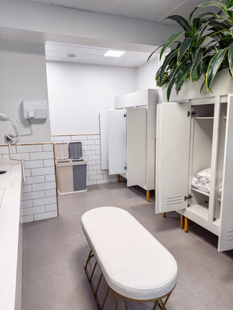 This changing room features sleek white lockers, a plush bench for seating, and decorative greenery, creating a clean and inviting atmosphere for users. Soft lighting enhances the modern design.の写真素材