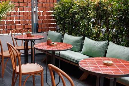 European restaurant or cafe. Outdoor seating with green cushions and red tiles, surrounded by plants, is bright and inviting.の写真素材