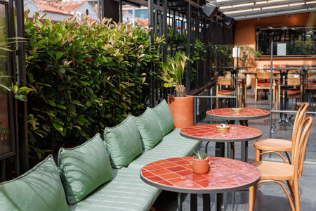 European restaurant or cafe. Outdoor seating with green cushions and red tiles, surrounded by plants, is bright and inviting.の写真素材