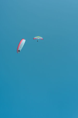 Paragliders glide gracefully above a vibrant blue sky, enjoying perfect flying conditions.