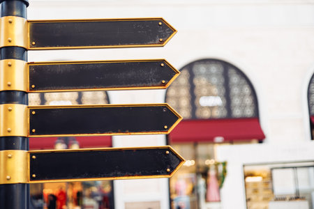 A well-crafted signpost displays multiple blank arrows, suggesting direction options for pedestrians in a vibrant shopping district filled with stores and activity. Sunlight enhances the scene.の写真素材