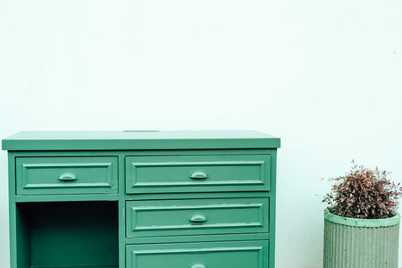 A green wooden dresser sits against a simple wall, featuring multiple drawers. Beside it, a...