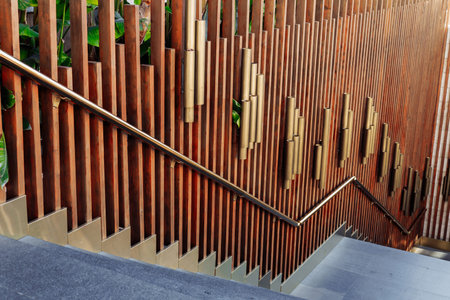 A beautifully crafted wooden stairway features vertical wooden slats and golden accents, surrounded by lush greenery. This architectural element showcases modern design in a city environment.の写真素材