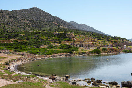 A serene landscape in Turkiye featuring a calm lake surrounded by green hills and rocky terrain. The clear blue sky enhances the natural beauty of the scene.の写真素材