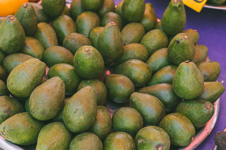 A pile of fresh, organic avocados displayed at a local market. The avocados are green and vary in size, showcasing their natural texture and color.の写真素材