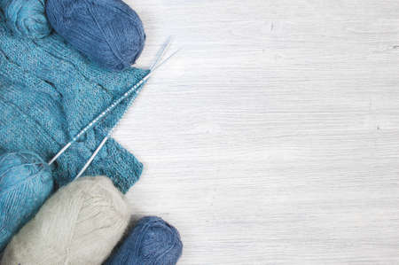 Knitted blue cloth and skeins of wool on the wooden tableの写真素材