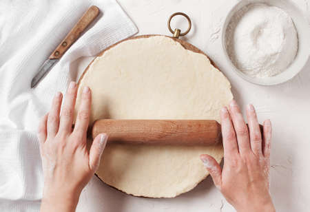Women's hands roll the dough on the kitchen tableの写真素材