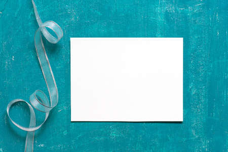 Painted aged blue background with blank sheet of paper and silver ribbonの写真素材