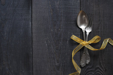 Vintage spoon and fork with golden ribbon on the old dark wooden tableの写真素材