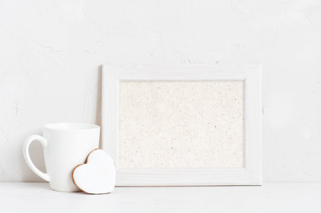 Horisontal empty white wooden frame, cup and cookie on the white background