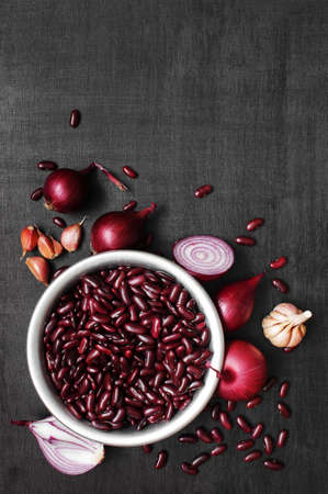 Beans on the metal bowl, onion and garlic on the black textured tableの写真素材