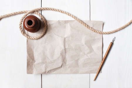 Empty crumple sheet of paper, inkpot, pen and rope on the white wooden tableの写真素材