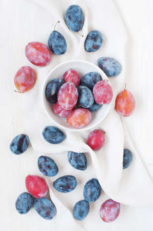 Wooden white table with plums and white towelの写真素材