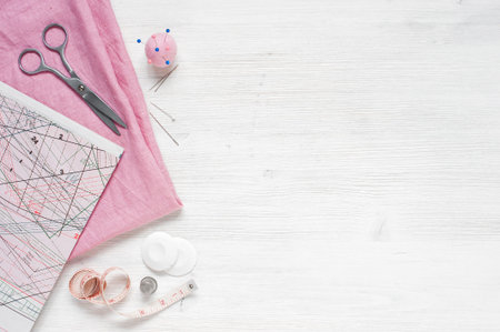 Pink natural fabric and sewing tools on  the white wooden table