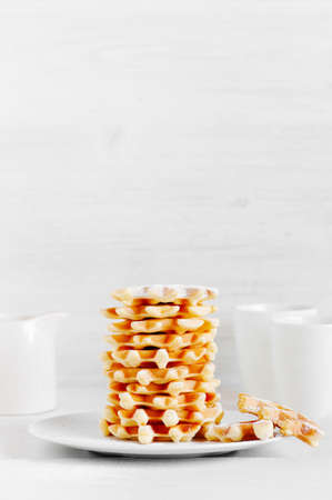 Stack of fresh waffles, mugs and jug with sause on the white wooden tableの写真素材