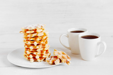 Stack of fresh waffles and two mugs on the white wooden table