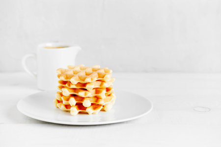 Stack of fresh waffles and jug with sause on the white wooden table