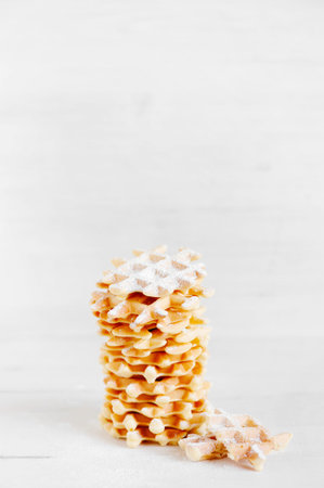 High stack of wafers with powdered sugar on the white wooden table