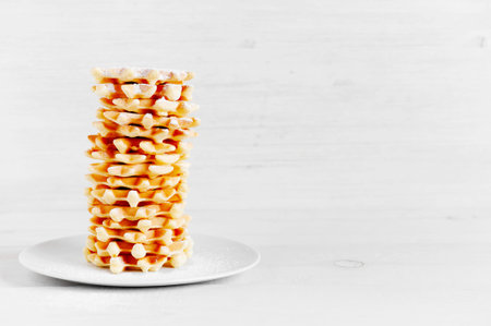 High stack of wafers sprinkled with powdered sugar on the white wooden table
