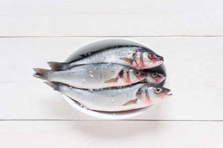 Fresh raw fish with salt on the white dish on the white wooden tableの写真素材