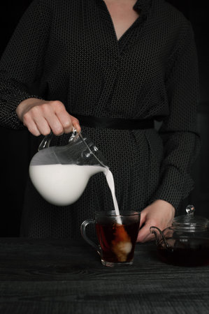 Woman pour milk in the cup of tea. Dark colors.